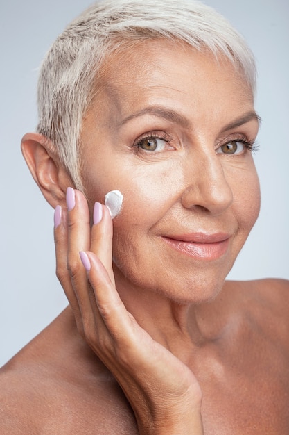 Photo beauté naturelle. jolie femme exprimant sa positivité tout en mettant de la crème sur son visage