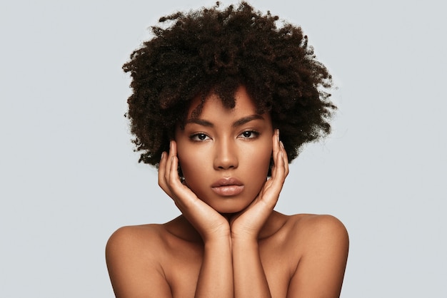 Beauté naturelle. Jolie jeune femme africaine regardant la caméra en se tenant debout sur fond gris