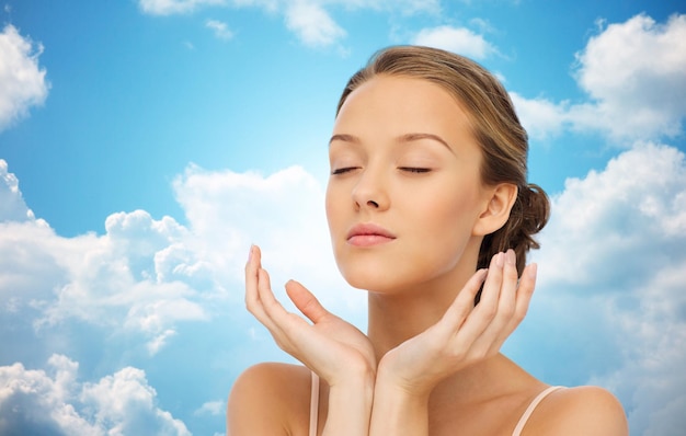 beauté, personnes, soins de la peau et concept de santé - jeune femme visage et mains sur fond bleu ciel et nuages