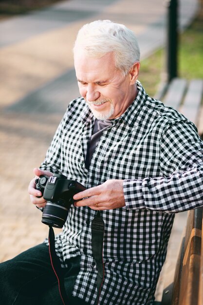 Beauté en photos. Vue de dessus de l'homme mûr rêveur utilisant la caméra et assis sur un banc