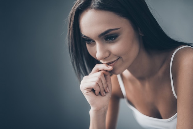 Beauté réfléchie. Jolie jeune femme tenant la main sur le menton et l'air réfléchie alors qu'elle était assise contre un mur gris