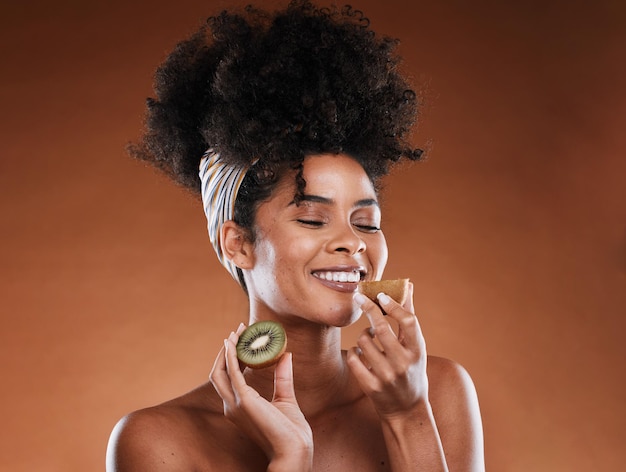 Beauté de soins de la peau et femme noire avec un kiwi en studio pour une routine naturelle organique et faciale Bonne odeur et modèle de fille africaine avec des fruits pour le traitement cosmétique de la peau isolé par fond marron