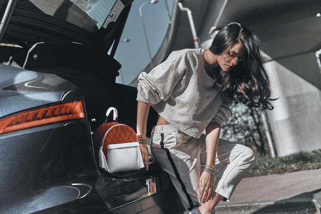 beauté et style. belle jeune femme ajustant sa chaussure tout en s'appuyant sur la voiture à l'extérieur