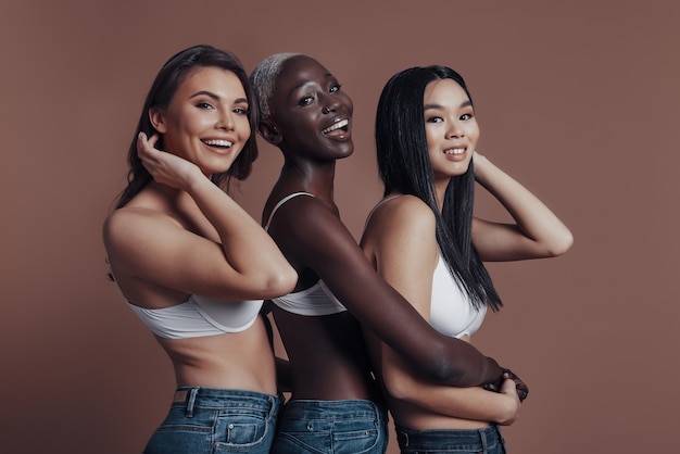 Beautés joyeuses. Trois jeunes femmes attirantes regardant la caméra et souriant