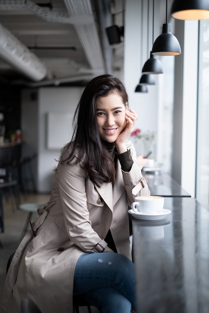 Photo beautiful portrait asian girl sitting on counter bar in coffee shop mettant la main sur son menton regardant la caméra avec le sourire.