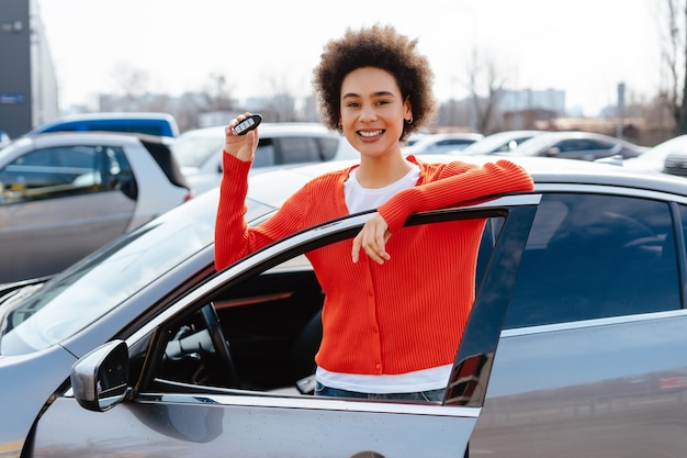 Photo beautiful smiling african american woman happy female owner holding car key standing near car