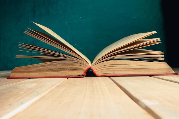 Beaux anciens livres ouverts sur une table en bois rouge et un fond de mur vert foncé derrière