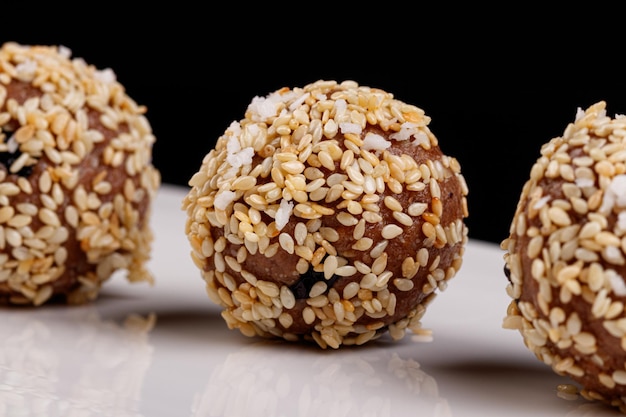 Beaux bonbons aux graines de sésame sur une plaque blanche sur fond noir