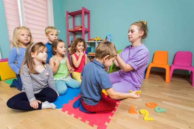 De beaux enfants d'âge préscolaire écoutent très attentivement le jeune enseignant