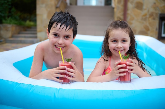 De beaux enfants caucasiens garçon et fille buvant un cocktail de fruits frais et sain tout en s'amusant dans une piscine d'eau