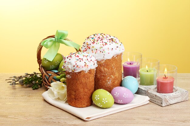 Beaux gâteaux de Pâques, oeufs colorés dans le panier et bougies sur table en bois sur l'espace jaune