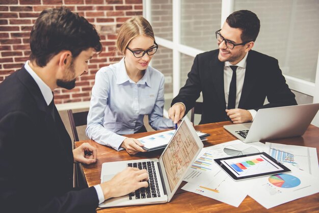 De beaux hommes d'affaires utilisent des ordinateurs portables pour étudier des documents, parler et sourire tout en travaillant au bureau