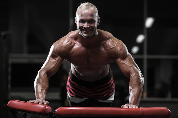 Beaux hommes athlétiques forts bodybuilder pompage des muscles avec des haltères