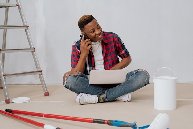 De beaux hommes sont assis avec un ordinateur portable sur les genoux dans une chambre située dans un appartement fraîchement peint