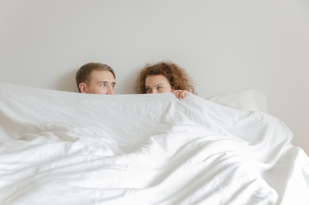 De beaux jeunes couples dormaient ensemble, se couvraient le visage de couvertures et se regardaient