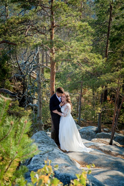 Beaux jeunes mariés étreignant sur fond de rochers et de montagnes. La mariée élégante et la belle mariée sont debout sur la falaise. Portrait de mariage. Photo de famille