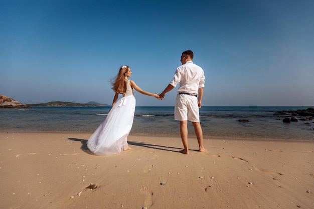 De beaux jeunes mariés se tenant la main en signe d'amour sur une plage de sable près des mers. Le mariage d'un jeune homme et d'une fille. Notion de mariage.