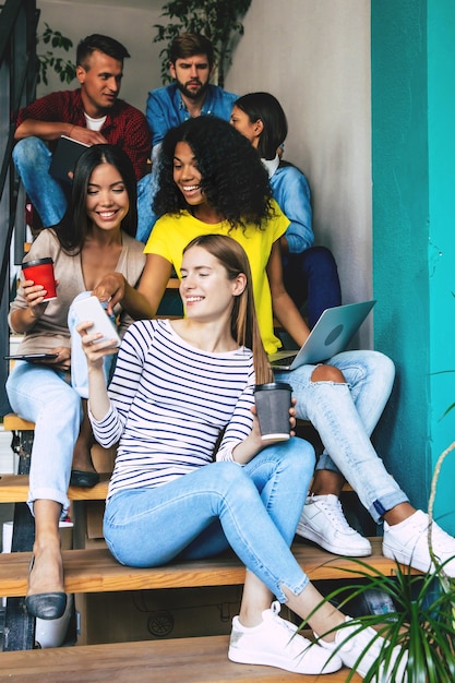 De beaux jeunes passent du temps ensemble. Les étudiants étudient à l'université. Lire un livre, travailler avec un ordinateur portable et communiquer en étant assis dans les escaliers