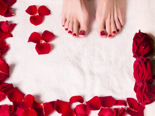 Beaux pieds féminins avec une belle pédicure sur une serviette éponge aux pétales de rose. Concept de spa et de soins de la peau.