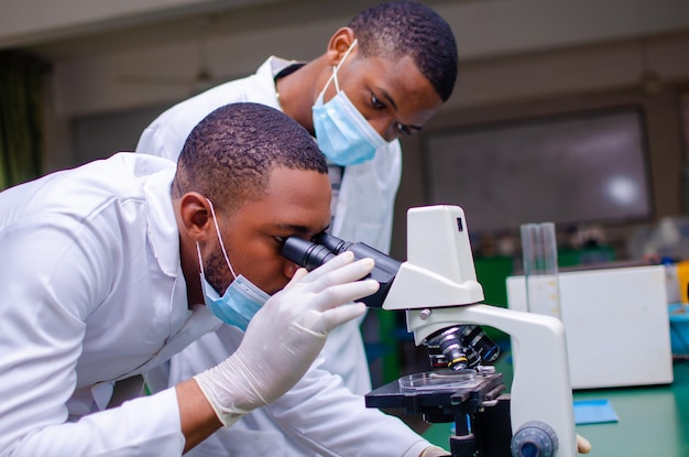 De beaux techniciens de laboratoire ou scientifiques afro-américains travaillant en laboratoire regardant à travers des microscopes