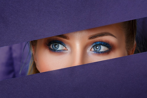 De beaux yeux de femmes regardent dans le trou de papier, un maquillage éclatant.