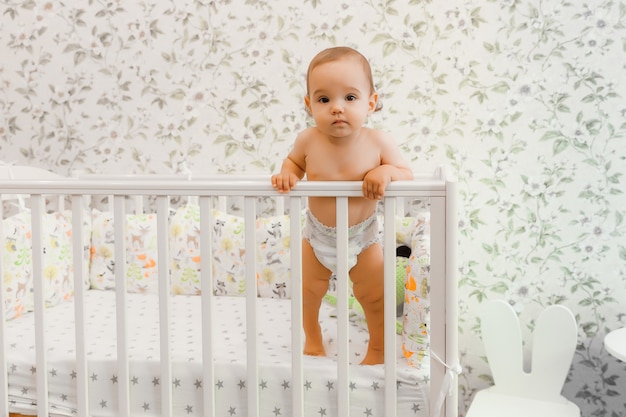 Un bébé de 11 mois dans une couche se tient dans son lit d'enfant dans le lit