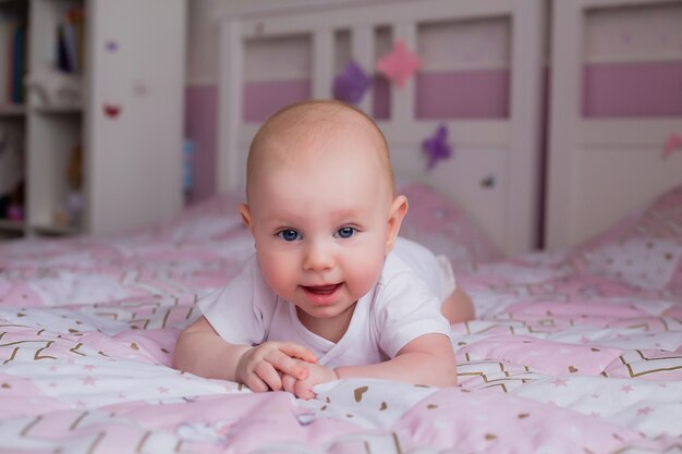 bébé 5 mois dans un body blanc allongé sur le lit avec une couverture rose