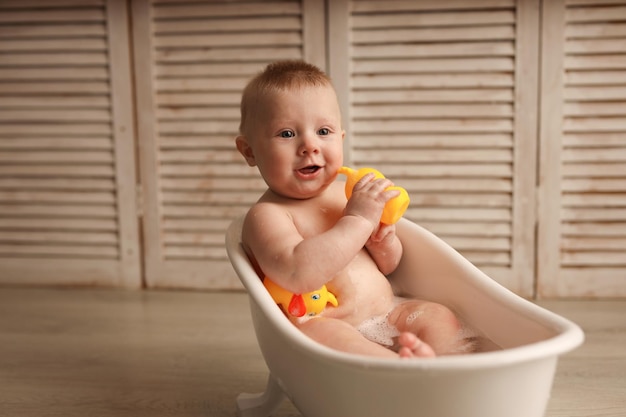 un bébé de 9 mois se baigne dans une baignoire blanche avec des canetons en caoutchouc