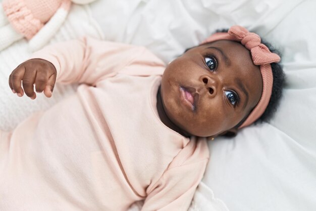 Bébé afro-américain allongé sur le lit avec une expression détendue dans la chambre