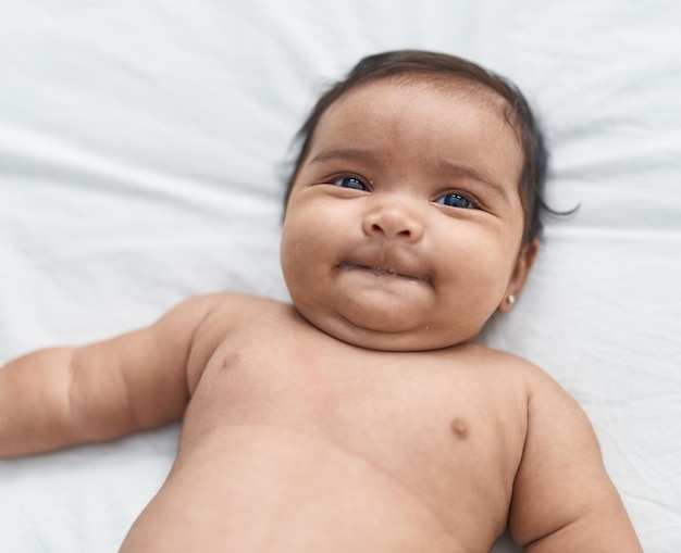 Bébé afro-américain souriant confiant allongé sur le lit dans la chambre