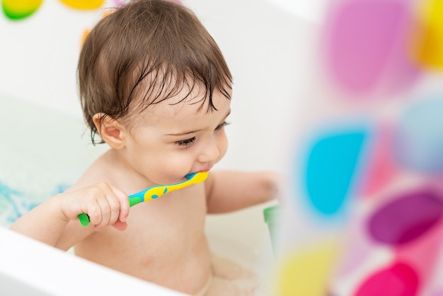 Un bébé d'un an se lave dans la baignoire joue avec des jouets apprend à se brosser les dents