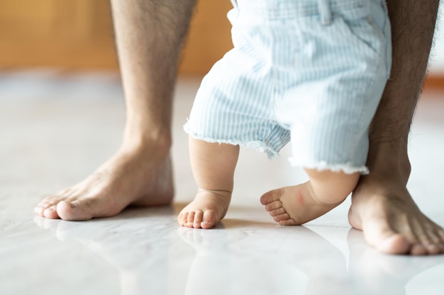 Bébé apprenant à marcher avec son père l'aidant à apprendre à la maison en se tenant la main