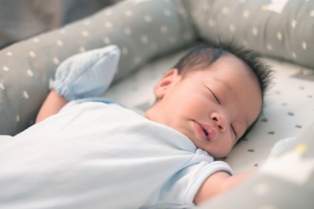 Bébé asiatique dormant sur le lit gris