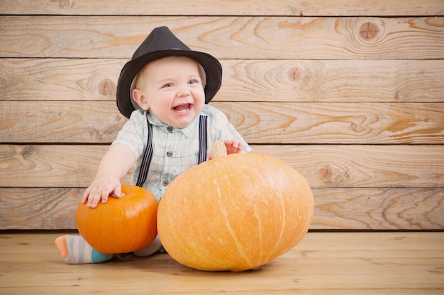 Bébé au chapeau noir avec des citrouilles sur fond de bois