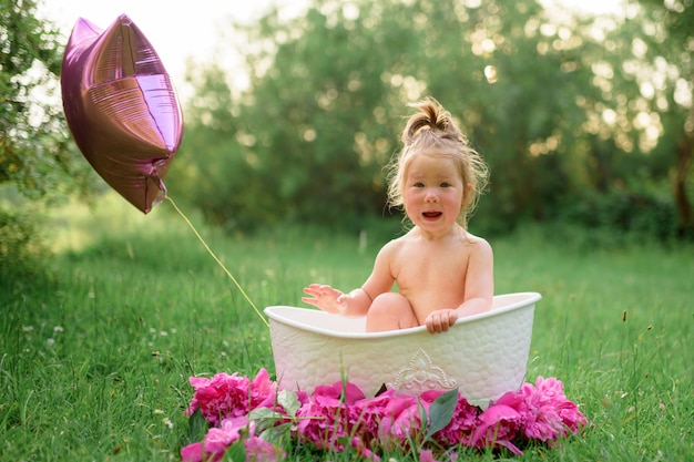 Bébé baigne dans un bain de lait dans la rue en été. La fille ouvrit la bouche de surprise.