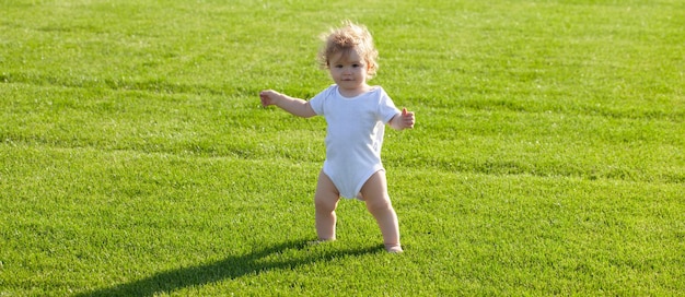 Bébé sur la bannière du champ d'herbe de printemps bébé debout pieds nus sur la pelouse verte enfant en bonne santé