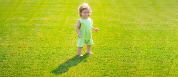 Bébé sur la bannière du champ d'herbe de printemps bébé debout pieds nus sur la pelouse verte petit garçon jouant dans le