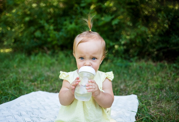 Bébé boit de l'eau au biberon dans la nature