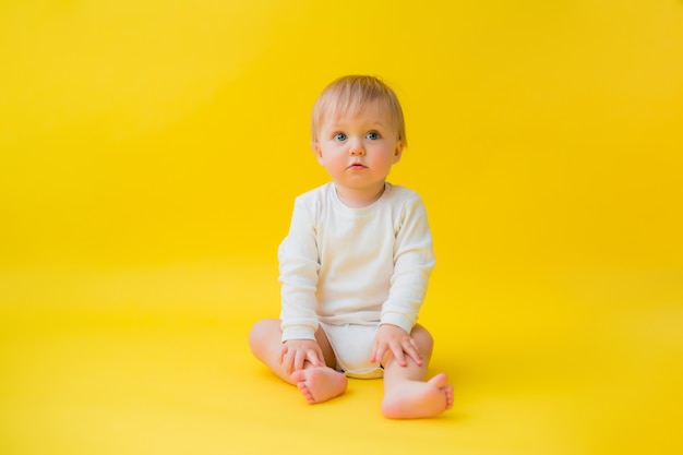 Bébé en bonne santé en body blanc est assis sur un fond jaune, espace pour le texte