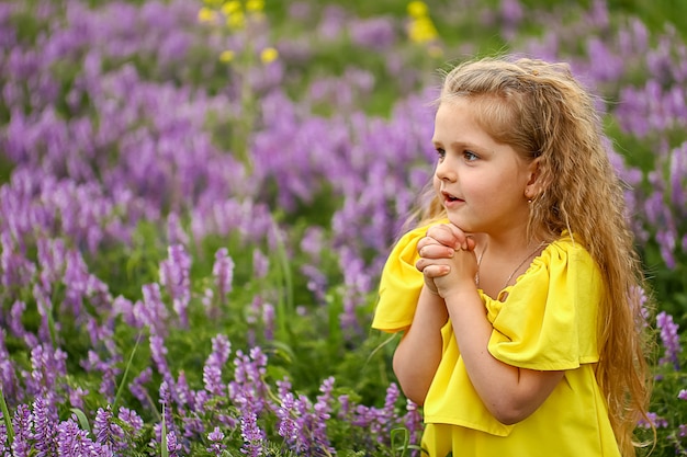 Bébé avec des boucles dans un champ de lavande, vêtue d'une robe d'été jaune, soirée d'été