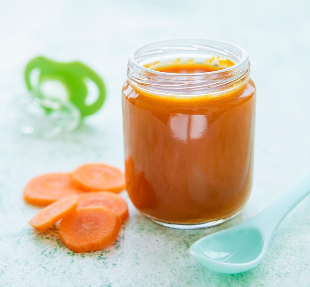 Bébé carotte en purée avec cuillère dans un bocal en verre, nourriture pour bébé