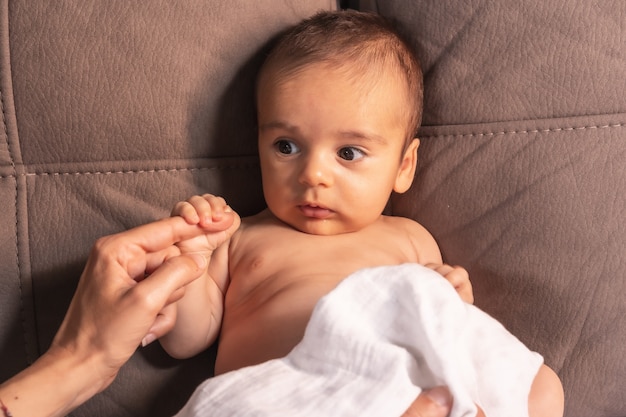 Bébé caucasien de deux mois assis sur un canapé tenant le doigt de sa mère. Photos de nouveau-né en studio