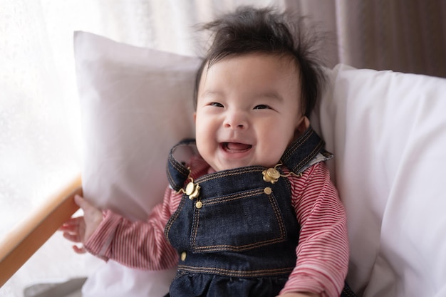Un bébé avec une chemise rayée rose et une salopette en jean sourit à la caméra.