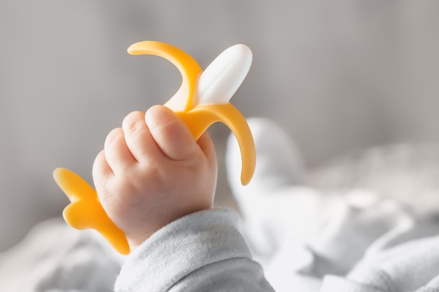 Photo un bébé de cinq mois tient un anneau de dentition banane dans sa main développement et massage des gencives gros plan anneau de dentition