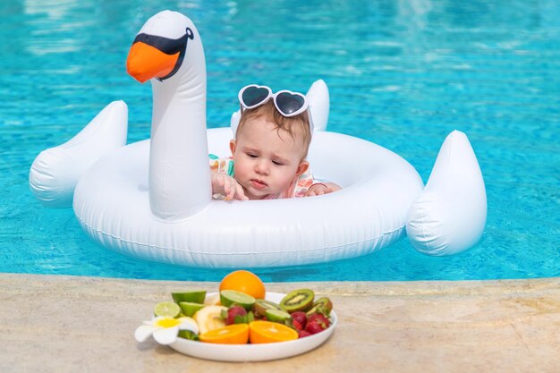 Photo bébé dans un anneau gonflable regardant une assiette de fruits