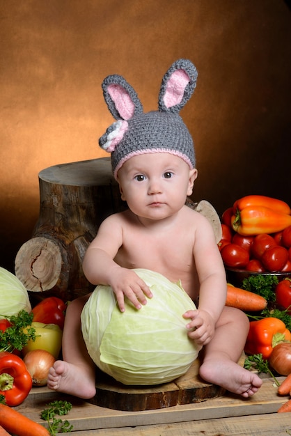 Bébé dans un costume de lapin avec des légumes sur un bois