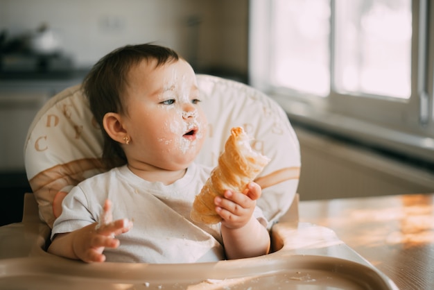 Bébé dans la cuisine mangeant avidement les délicieuses cornes de crème, remplies d'une crème à la vanille