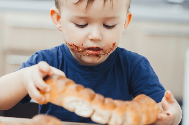 Bébé dans la cuisine mangeant un gros pain ou une tarte au chocolat