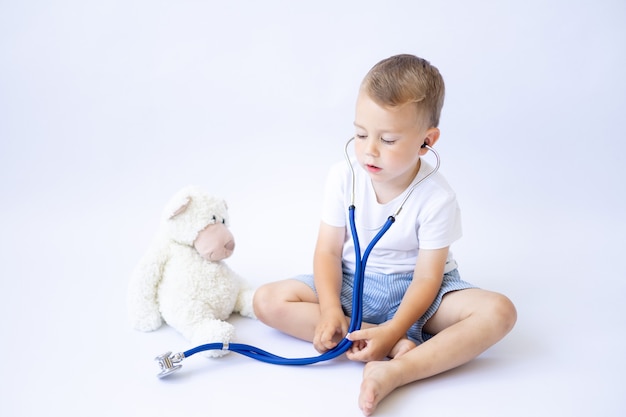 Un bébé dans un masque médical est assis avec un stéthoscope et traite une pandémie d'isolat de fond blanc en peluche