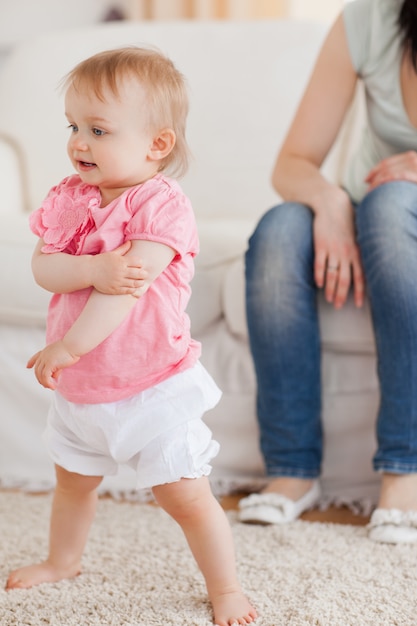 Bébé debout sur un tapis alors que sa mère est assise sur un canapé